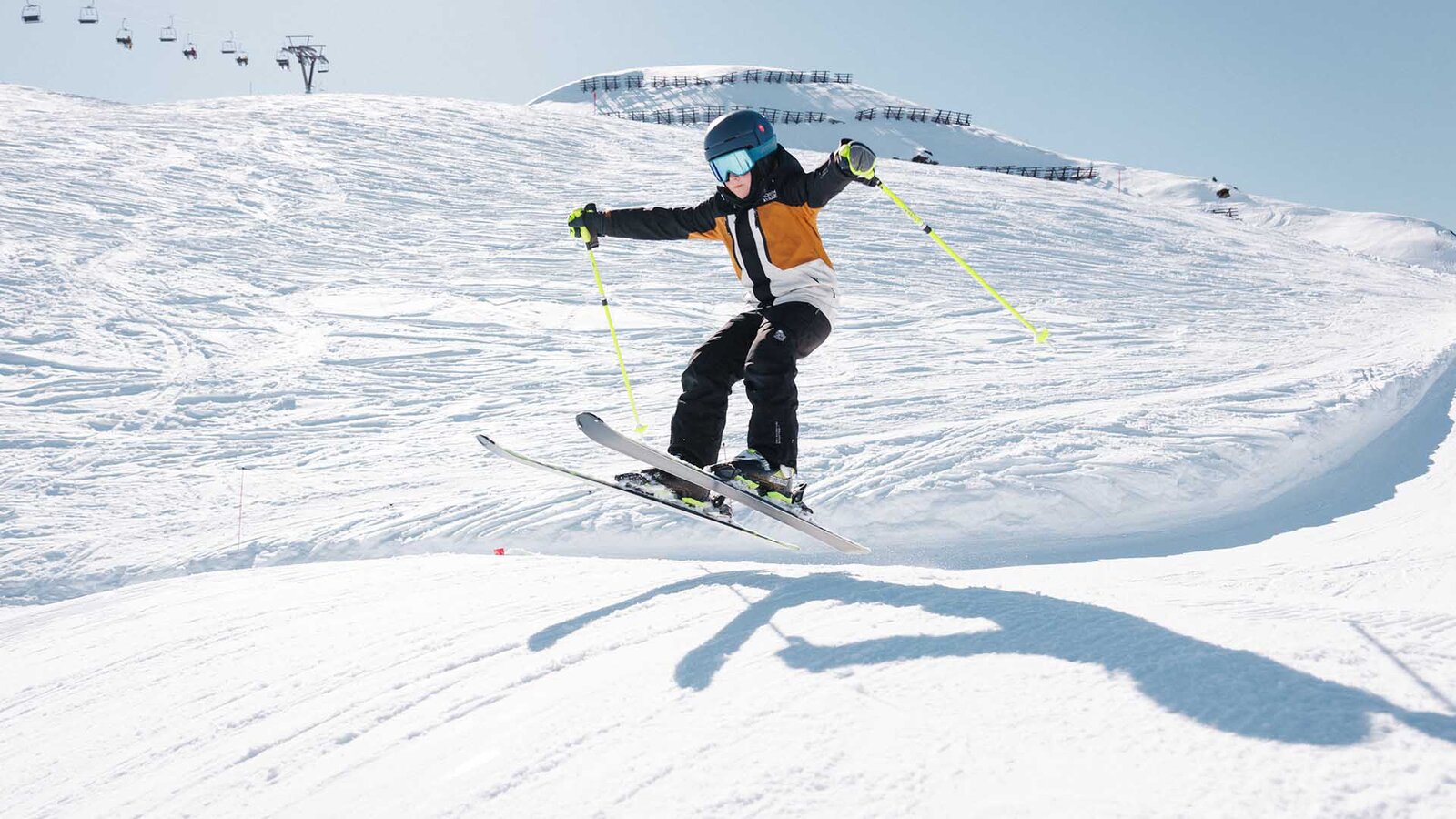 Skifahrer springt mit angewinkelten Knien und ausgestreckten Armen auf schneebedeckter Piste