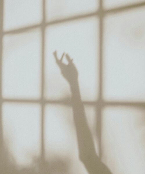 Schatten einer ausgestreckten Hand vor einem Fenster mit quadratischen Scheiben